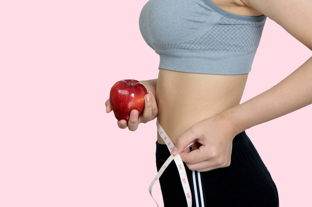 lichaam van de slanke vrouw met apple fruit geïsoleerd op roze achtergrond wit - Foto, afbeelding