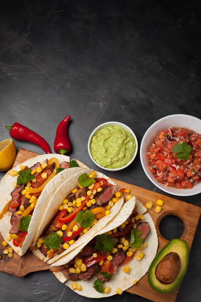 霜降り牛、ブラックアンガス暗い石の背景に木の板に野菜と 3 つのメキシコのタコス。ソース ワカモレとサルサの鉢でメキシコ料理。コピー スペース平面図 - 写真・画像