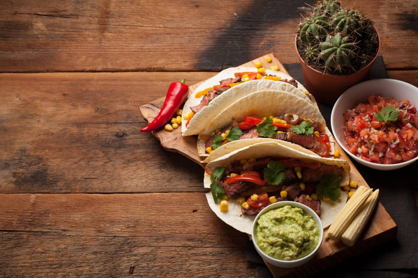 drei mexikanische Tacos mit marmoriertem Rindfleisch, schwarzem Angus und Gemüse auf einem alten rustikalen Tisch. mexikanisches Gericht mit Soßen Guacamole und Salsa in Schüsseln. Ansicht von oben mit Kopierraum - Foto, Bild