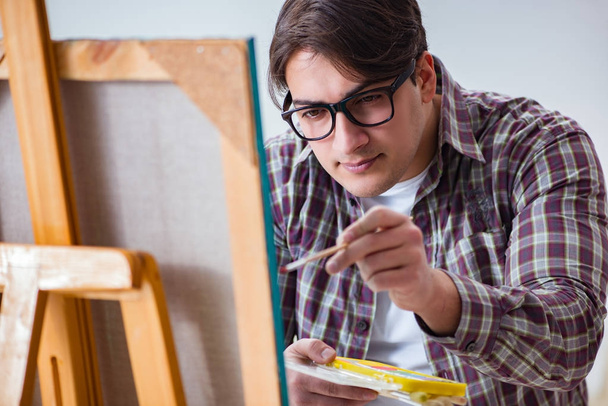 Νεαρός αρσενικός καλλιτέχνης ζωγραφίζει σε φωτεινό στούντιο - Φωτογραφία, εικόνα