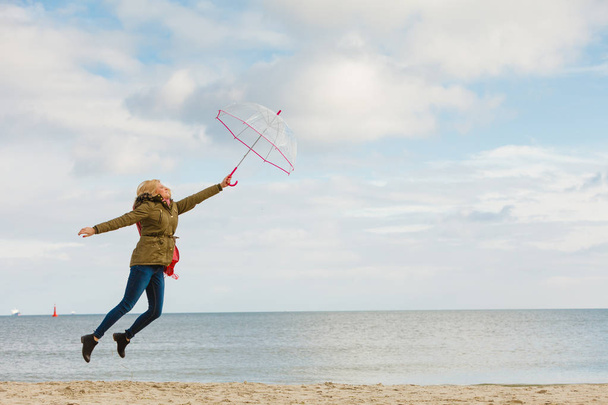 Nainen hyppääminen läpinäkyvä sateenvarjo rannalla
 - Valokuva, kuva
