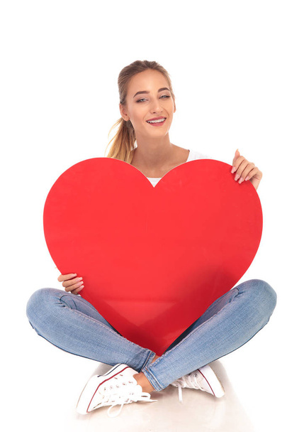 Смеющаяся молодая женщина с брекетами, держащая большое красное сердце
  - Фото, изображение