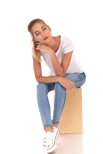 pensive young casual woman sitting on wooden box  - Photo, Image