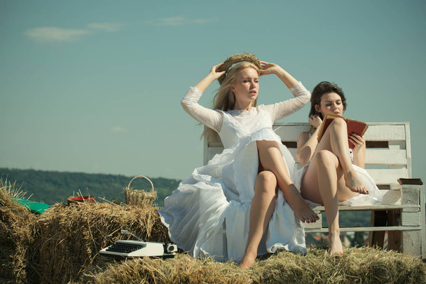 Two girls sitting on bench on hay. - Фото, зображення