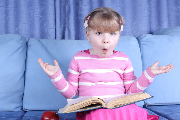 Menina surpreendida com maçã e livros no sofá
 - Foto, Imagem