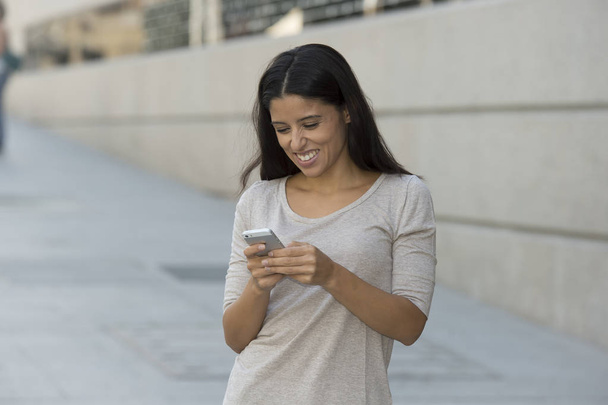 молодая красивая и счастливая латинская женщина на фоне городской улицы с помощью интернета на мобильном телефоне смс
 - Фото, изображение