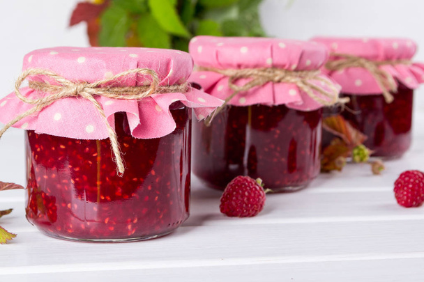 Jars with raspberry jam placed in rows and fresh raspberry - Photo, Image