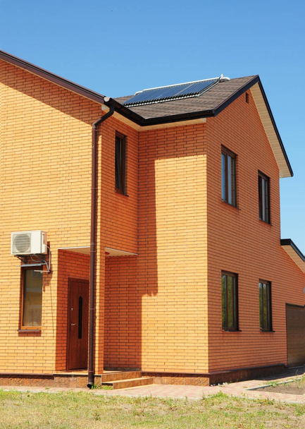  アスファルト鉄片屋根雨樋システムと太陽電池パネル、真空太陽熱給湯システム。エネルギー効率化屋根の建設とれんが造りの家. - 写真・画像