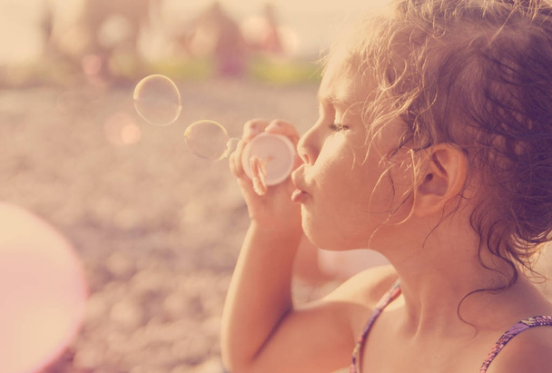 Viisivuotias kaunis pieni tyttö puhaltaa saippuakuplia auringossa
 - Valokuva, kuva