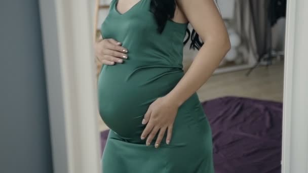 Pregnant woman at 7 months pregnant stands at the mirror and gently strokes her abdomen - Footage, Video