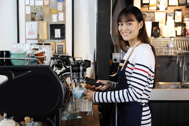 Smiling asian barista preparing cappuccino with coffee machine.  - Fotó, kép