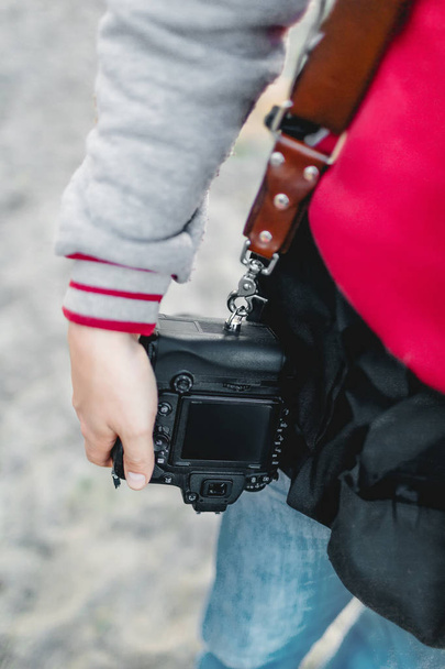 Photo camera on a leather strap. Photographer holds a camera in the hand. Close-up. A - Foto, Imagen