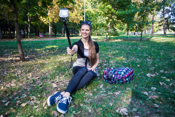 Nuori kaunis tyttö istuu nurmikolla ja ottaa selfie toiminta kamera
 - Valokuva, kuva