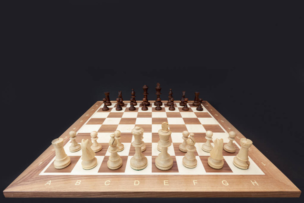 Chess pieces on the board. Black wood background behind. - Fotoğraf, Görsel