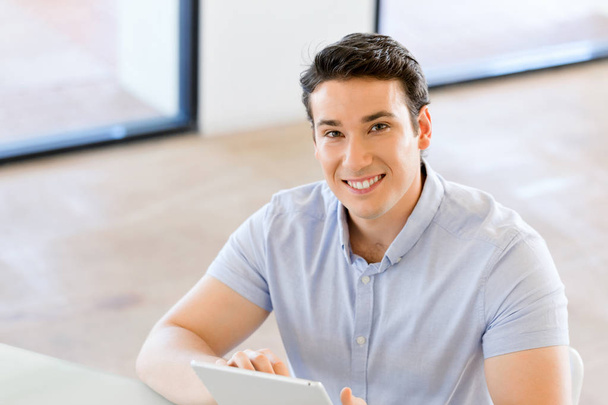 Young handsome businessman using his touchpad sitting in office - Photo, Image