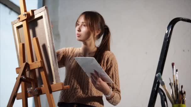 Een tiener schildert een schilderij met verf op doek, dat op een ezel staat - Video