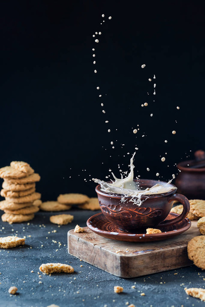 Левітація молока бризкає в глиняній чашці, з печивом на темній руїні
 - Фото, зображення