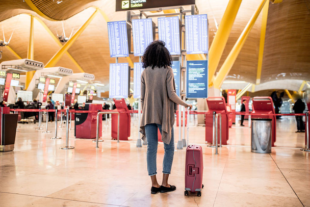 Γυναίκα ψάχνει στο πίνακα πληροφοριών χρονοδιαγράμματος στο αεροδρόμιο με μια βαλίτσα - Φωτογραφία, εικόνα