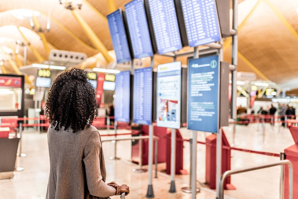Kobieta, patrząc na panelu informacje harmonogramu na lotnisku z walizką - Zdjęcie, obraz