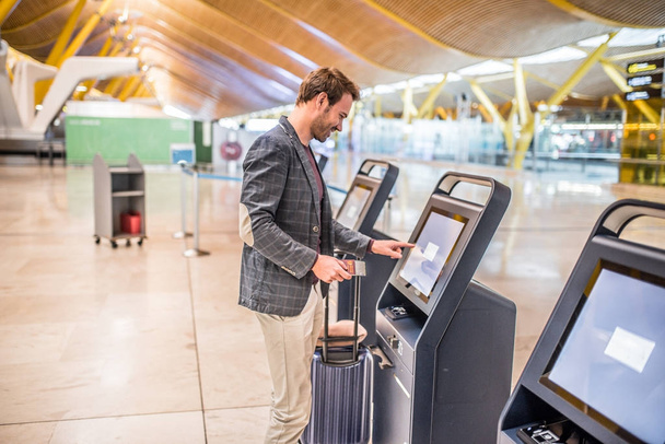ευτυχισμένος άνθρωπος χρησιμοποιώντας το μηχάνημα check in του αεροδρομίου να πάρει την κάρτα επιβίβασης. - Φωτογραφία, εικόνα