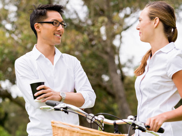 Retrato de casal sorridente em pé no parque com a bicicleta conversando
 - Foto, Imagem