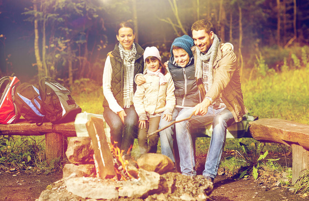 happy family sitting on bench at camp fire - 写真・画像
