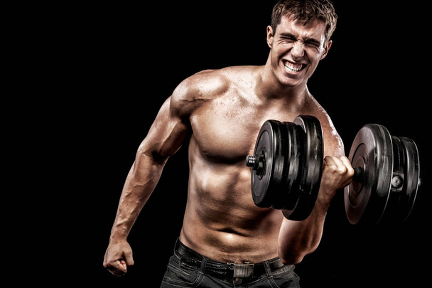 Athletic shirtless young sports man - fitness model holds the dumbbell in gym. Copy space fore your text. - Foto, imagen