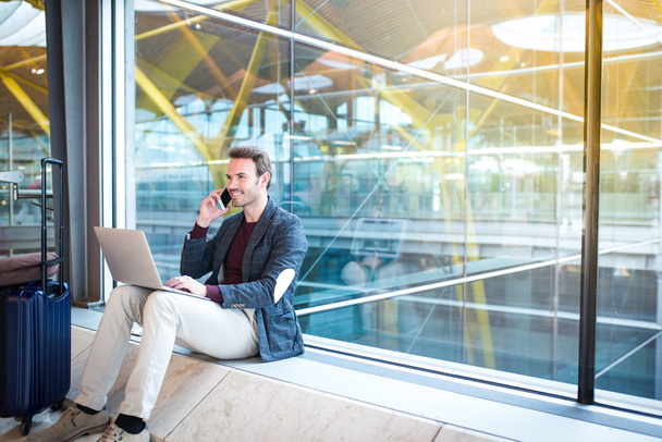 homme assis à l'aéroport en utilisant un ordinateur portable et un téléphone portable à côté de la fenêtre
. - Photo, image