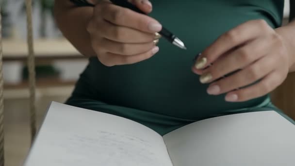 A young woman writes a note with a black pen in a notebook - Video, Çekim