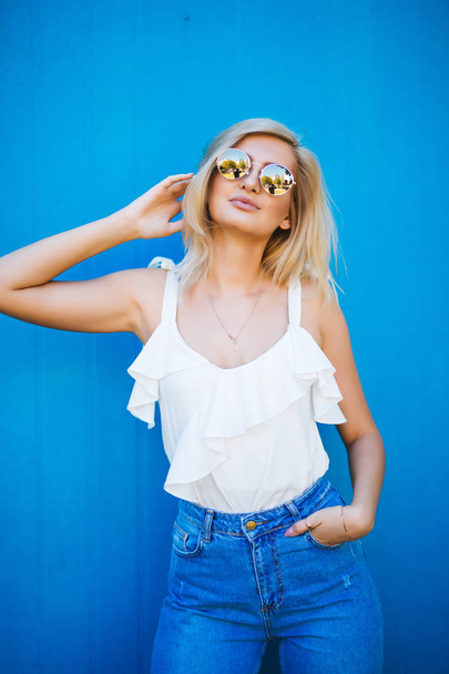 Блондинка з білою сорочкою і сонцезахисними окулярами на синьому фоні
 - Фото, зображення