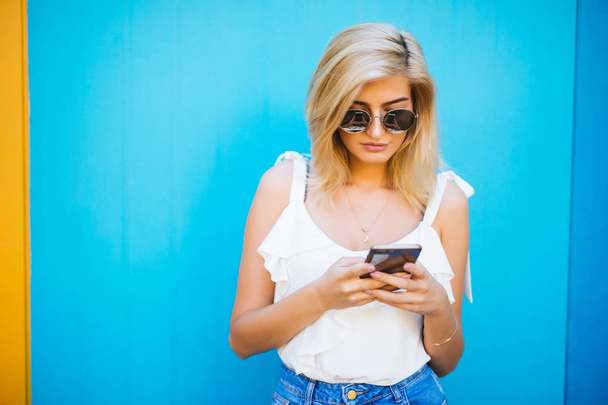 Mujer hermosa joven usando estudio de teléfono móvil sobre fondo de color azul
 - Foto, Imagen