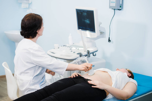 Mujer embarazada que mira las inyecciones de ultrasonido de su bebé en crecimiento mostradas por su médico durante el examen médico
 - Foto, imagen