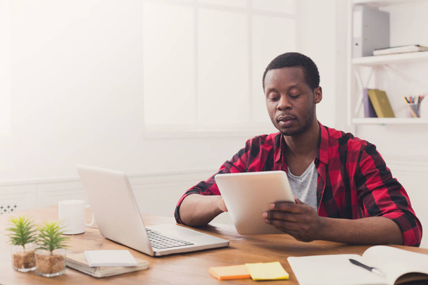 Homme d'affaires noir dans un bureau décontracté, travailler à la fois sur ordinateur portable et tabl
 - Photo, image