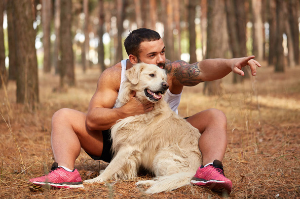 Handsome young man with a labrador outdoors in the forest. - Foto, afbeelding