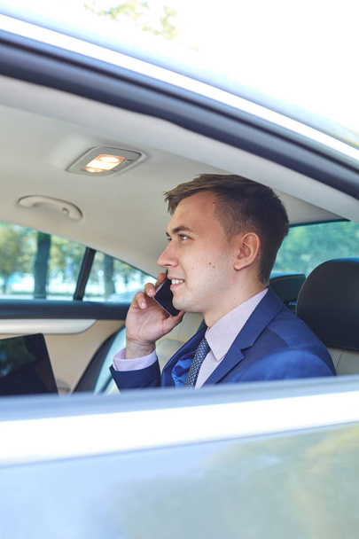 Businessman in his car with a laptop talking on the phone - Photo, Image