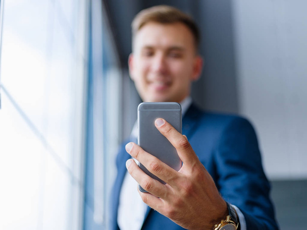 Close-up of an office worker holding a phone on a blurred background. Man taking a selfie. New phone concept. - Photo, Image