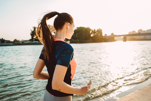 a girl in a sportive uniform performs an evening run along the river - Foto, imagen