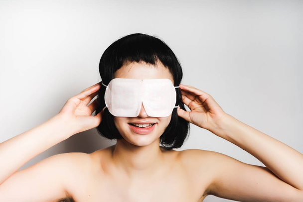 lovely girl with black short hair puts on a mask for sleep - Foto, Bild