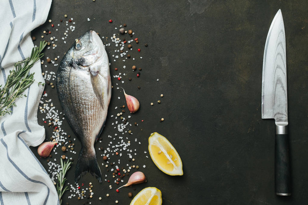 Fresh fish with salt, pepper, aromatic herbs and vegetables over vintage dark background . - 写真・画像