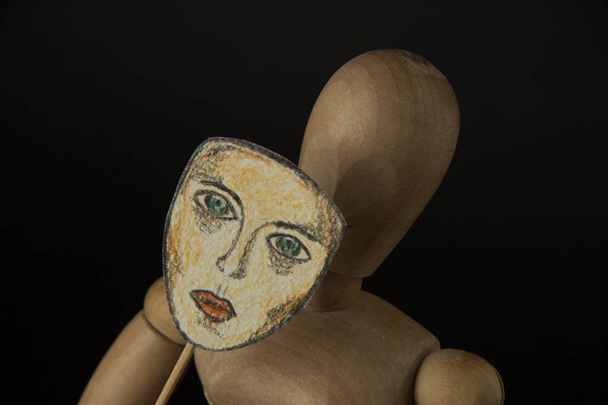 Muñeca de madera en bisagras sostiene una máscara en las manos y cubre su cara
  - Foto, imagen