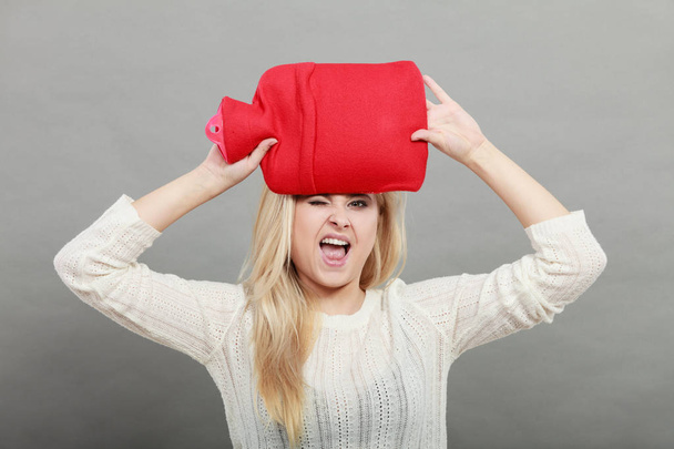 Woman holding red hot water bottle on head - Foto, Bild