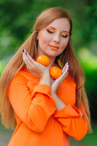 Portrait of pretty red hair woman with juicy delicious mandarins at summer green park. - Photo, Image