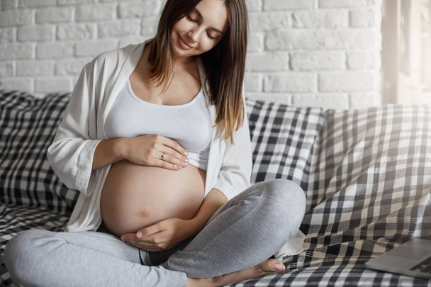 Beautiful pregnant lady caring of her tummy listening for her fetus sitting home. Having a wealthy husband is a key to easy pregnancy. - Photo, image