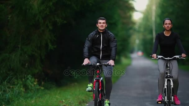 Handsome szakállas profi férfi kerékpáros a verseny kerékpár lovaglás reggel együtt barátnőjével, mindkét viselt védősisakok és a szemüveg, nap, közöttük átszűrődő. - Felvétel, videó