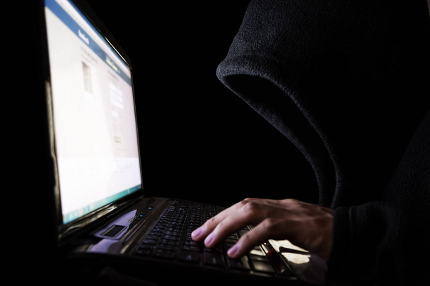 Hacker no identificado en Black Hood usando Computadora Portátil. Enfoque selectivo
 - Foto, Imagen