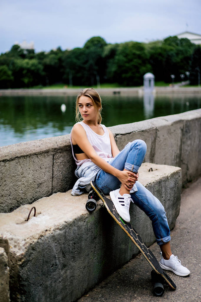 Girl on quay sitting with longboard - Фото, изображение