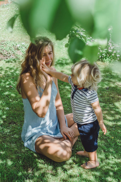 cute blonde boy with young mother on green grass outdoor - Fotó, kép
