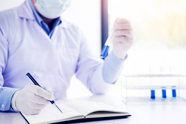 Scientist in white coat holding and examining test tube with rea - Photo, Image