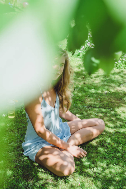 cute blonde woman at blue dress sitting on green grass outdoor at summer - Фото, зображення