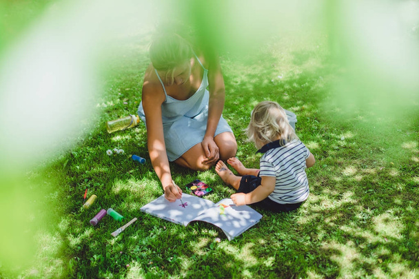 cute blonde boy with young mother drawing on green grass outdoor - Foto, immagini